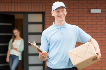 Smiling courier in uniform holding package and delivering it to recipient