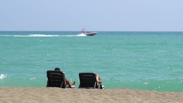 Young Couple Lying On A Lounge Chair On The Beach Watching