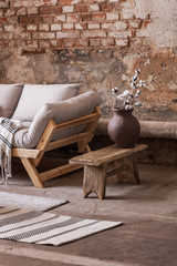Fototapeta na wymiar Flowers on wooden stool next to beige sofa in living room interior with red brick wall. Real photo