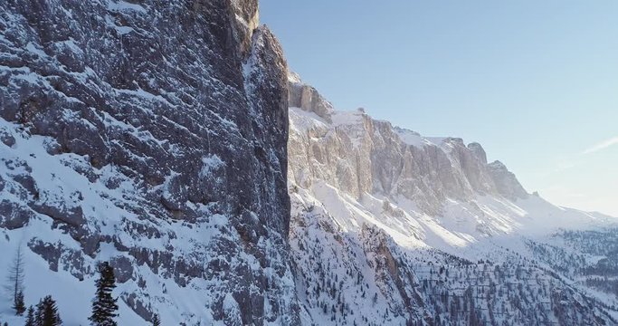 Forward aerial along snowy alpine steep rocky cliff valley.Sunny day,clear sky.Winter Dolomites Italian Alps mountains outdoor nature establisher.4k drone flight