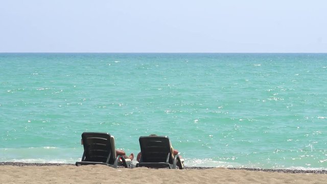 Young Couple Lying On A Lounge Chair On The Beach Watching