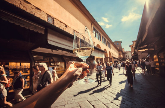 Wine glass in hand of tourist over crowd between old buildings of Florence, Tuscany. Ancient city in Italy. UNESCO World Heritage Site