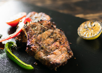Grilled meat served with vegetables, spices on a slate plate.