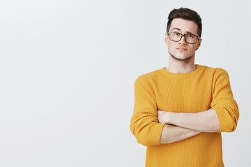 Displeased guy waiting for explanations. Confused doubtful and dissatisfied young handsome caucasian male in yellow sweater and glasses crossing hands on chest in hesitation and uncertainty - obrazy, fototapety, plakaty