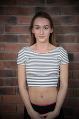 Portrait of young beautiful woman in crop top with long hair on brick wall background