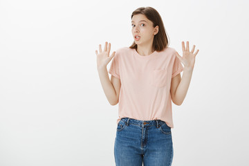 It was not my fault, I have nothing to deal with it. Confused innocent attractive female friend in casual clothes, raising palms in surrender, standing surprised and clueless over gray background