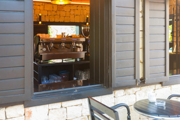 A small coffee shop in traditional French style. Exterior of a building with a coffee table outside. The walls are made of sandstone and black fill the open windows.