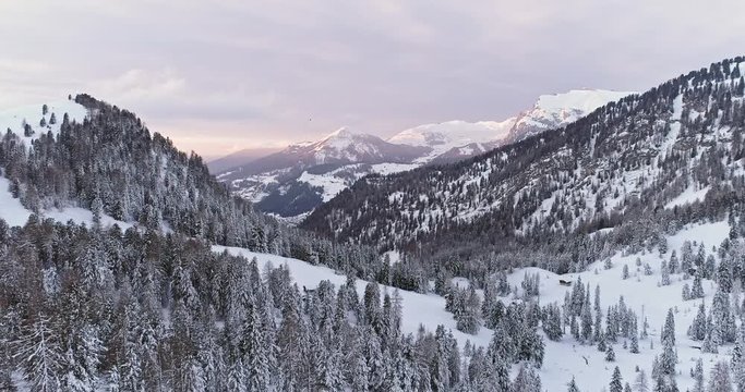 Forward aerial to snowy valley with woods forest at Sella pass.Sunset or sunrise,cloudy sky.Winter Dolomites Italian Alps mountains outdoor nature establisher.4k drone flight