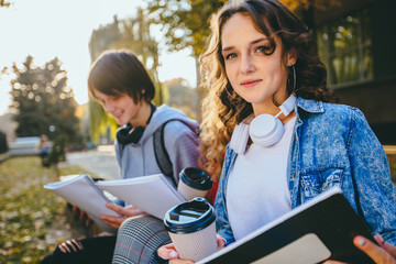 Two male and female hipster students studying reading notes drinking coffee together outdoors...