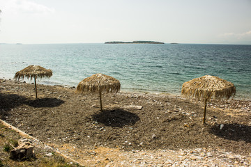 three straw umbrellas on shore line of Mediterranean near sea, summer hot weather