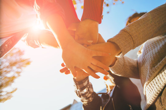 A group of four friends students man and women handshake high five teamwork concept of tenagers friendship, sunny autumn mood . Bottom view