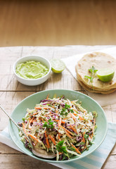Coleslaw made from cabbage, carrots and various herbs, served with tortillas and guacamala on a wooden background.