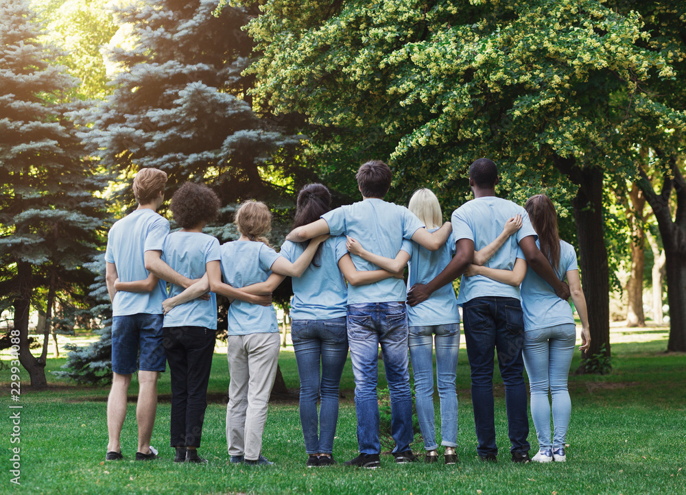 Wall mural Group of happy volunteers embracing in park