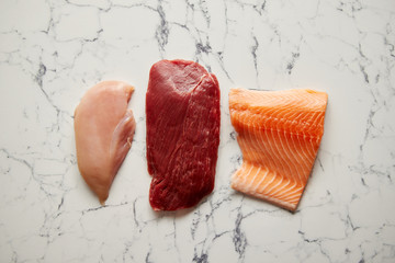 Assortment of fresh raw beef steak, chicken breast, and salmon fillet. Top view composition on...