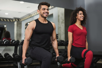 Diverse couple training with dumbbells in gym