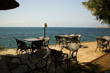 open air patio cafe furniture tables and chairs on shore line of tropic Mediterranean sea in summer hot weather time