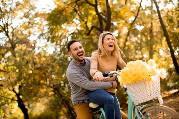 Active young couple enjoying riding bicycle in golden autumn park