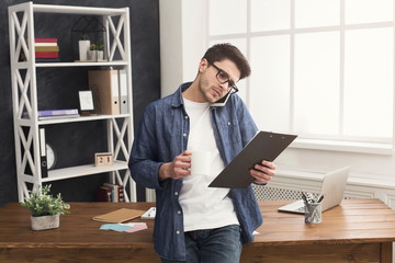 Fototapeta premium Pensive young businessman talking on mobile and reading documents