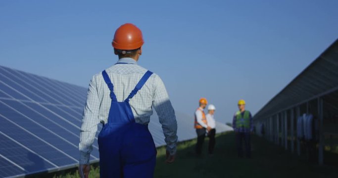 Medium shot from behind of an electrical technician walking with a tablet inbetween long rows of photovoltaic solar panels