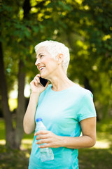 Sporty senior woman using mobile phone in the park