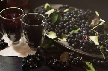 Two glasses fresh juice from black chokeberry berries ( Aronia melanocarpa ) near branches with black berries. Horizontal.