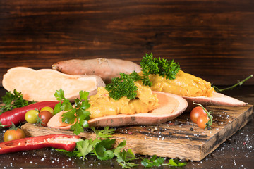 Mashed sweet potato with pepers chilli, tomatoes and greenery on a dark wooden board background. Horizontal.