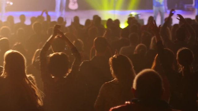 Audience cheerfully applauds clapping hands at the concert flashing spotlights to performer