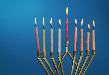 The lit of hanukkah candles in menorah on blue background