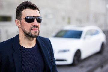 close up portrait of handsome business man in sunglasses posing with his car