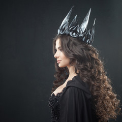 Portrait of a Gothic Princess. Beautiful young brunette woman in metal crown and black cloak.