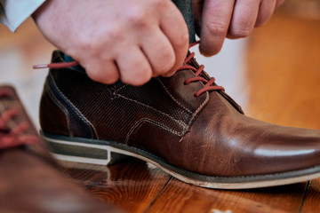 Grooms fastening shoe laces on stylish brown leather shoes on wedding day
