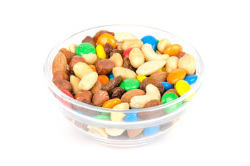 Trail mix in glass bowl. Snack mix. Almonds, cashews, peanuts, hazelnuts, raisins and colorful chocolate candies. Food to be taken along hikes. Macro food photo closeup from above on white background.