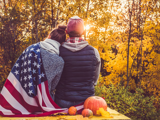 Happy married couple holding the US flag against the background of yellow trees and the setting sun. Happy relationship concept