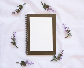 Flat lay style of blank card on notebook with flowers decorated on white cloth, top view