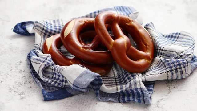 Three german fresh baked pretzel buns placed on white and blue checkered napkin. Stone background. Shot from above.