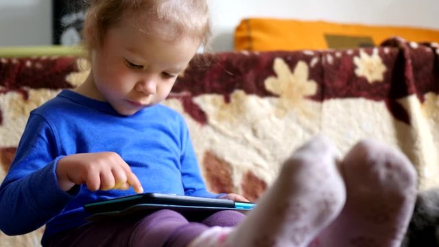 Little girl on a couch playing tablet computer game sliding touchscreen