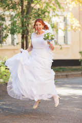 Fototapeta na wymiar Beautiful redhead bride with bouquet outdoor. Happy bride jumping and having fun outdoors. Beautiful bride posing in her wedding
