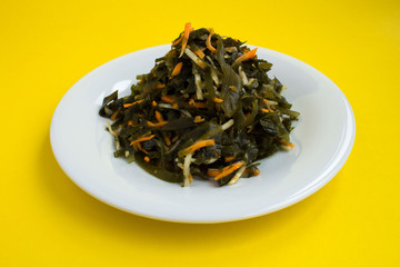 Salad with seaweed, celery and carrots in the  white plate on the yellow background