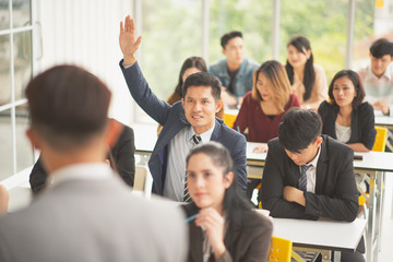 Man speaker talking in front of seminar meeting room with many audiences for business concept, some audiences raising up hand for asking in question and answer time in meeting room