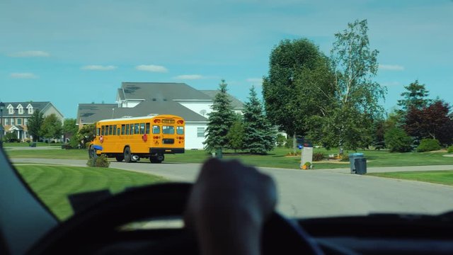View from the window of the car, which goes after the school yellow school bus in the US suburb