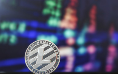 One Litecoin coin on a background of red and green stock market figures