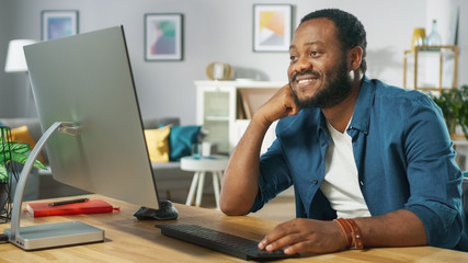 Obraz premium Portrait of the Happy Man Sitting at His Desk, Watching Videos at Home. In the Background Cozy Living Room.