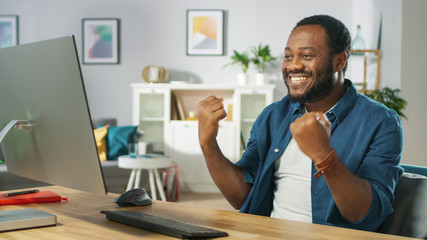 Fototapeta premium Happy Young Man Uses Personal Computer at Home, Wins Big, Does 