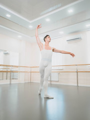 Young handsome male dancer practicing in classical ballet in small studio with mirrors. Man in white tights. Professional choreographer is working on creating performance