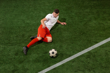 Football player tackling for ball over green grass background. Professional football soccer player in motion at studio. Fit jumping man in action, jump, movement at game.