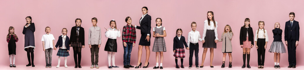 Obraz premium Cute smiling happy stylish children and female teacher on pink background. Beautiful stylish teen girls and boy standing together and posing at studio. Classic style. Kids fashion and emotions concept
