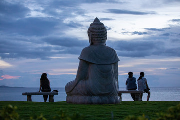 Statue of Buddha and three your woman watching sunset over Pacific ocean