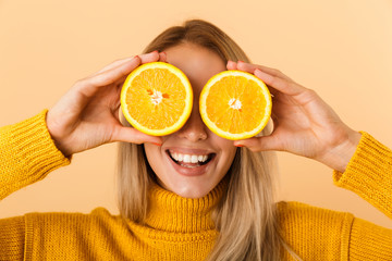 Beautiful woman covering eyes with citrus lemons posing isolated over yellow wall background.