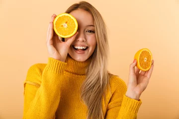 Fotobehang Beautiful woman covering eyes with citrus lemons posing isolated over yellow wall background. © Drobot Dean