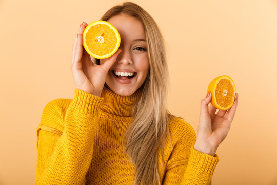 Beautiful woman covering eyes with citrus lemons posing isolated over yellow wall background.